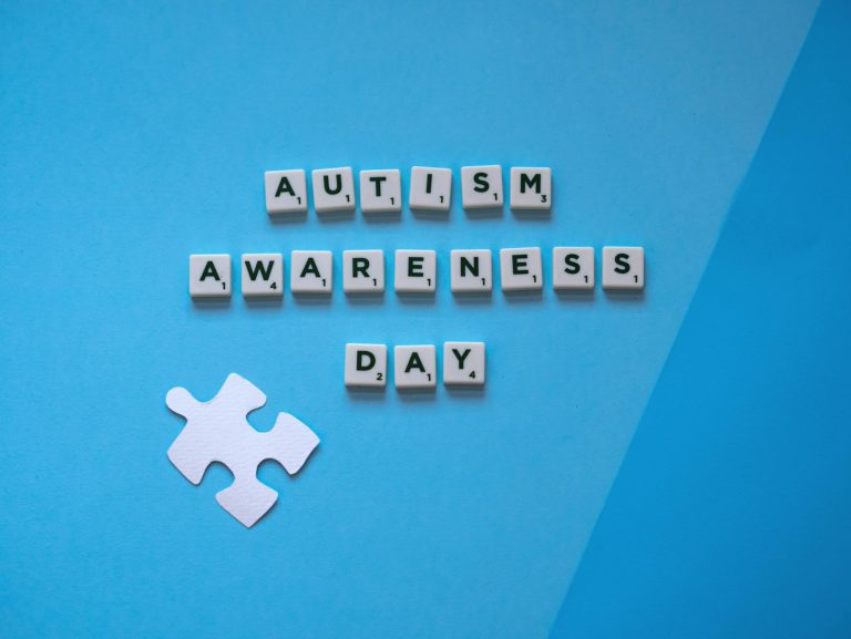 Autism Awareness Day concept with letter tiles and a puzzle piece on a blue background.